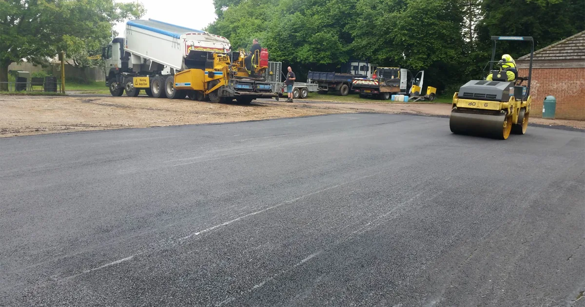 Surfacing crew, paver and roller working on a large asphalt area