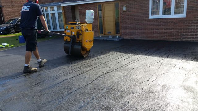 Pedestrian roller finishing asphalt outside a house