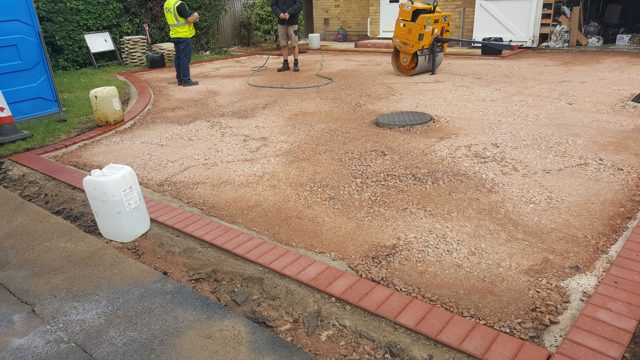 Roller compacting a driveway base around an access cover
