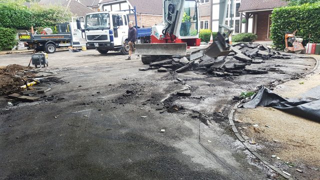 Excavator lifting broken sections of old tarmac