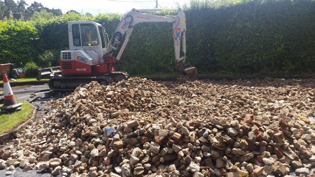 Excavator spreading coarse aggregate for a driveway base